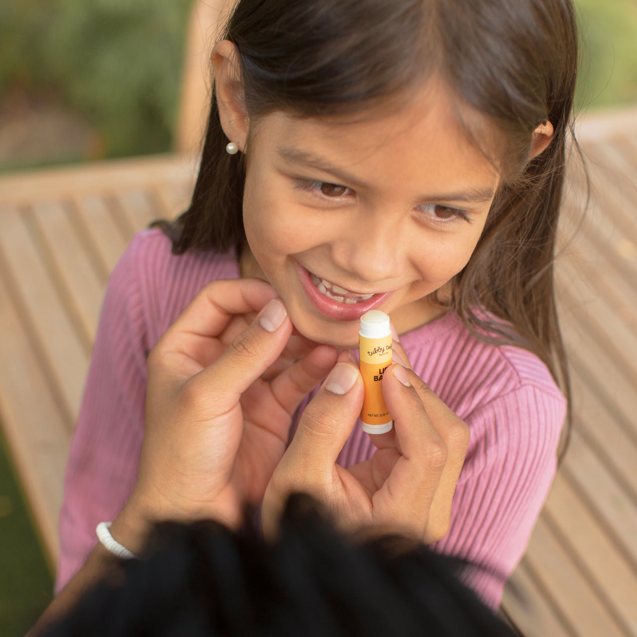 Child receiving lip balm from an adult outdoors